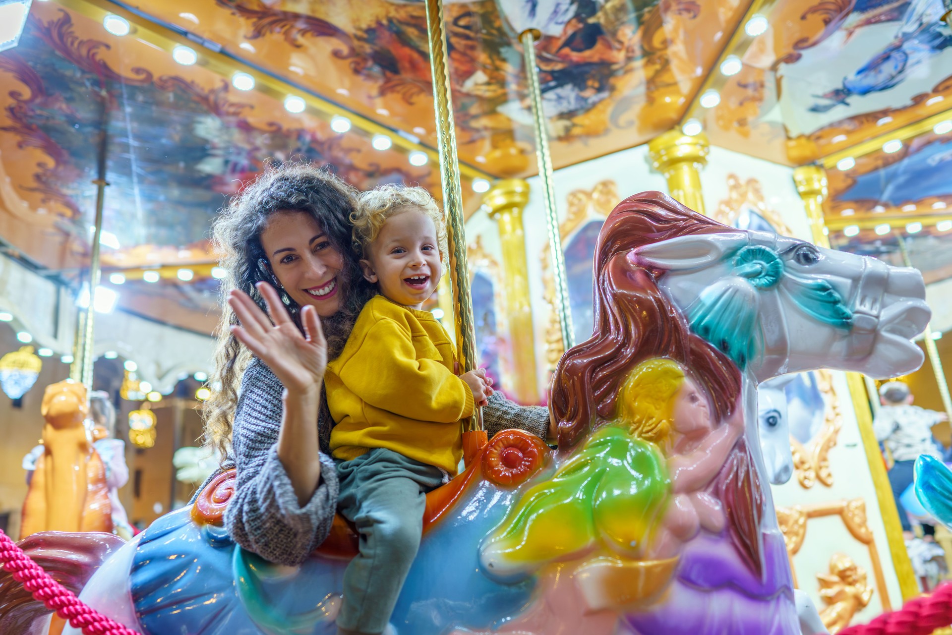 Mother and son waving while riding carousel horse